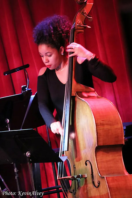 Aneesa Strings performs on upright bass with a red curtain backdrop.