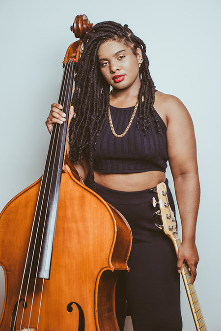 Endea Owens poses with her upright bass, with an electric bass visible as well.