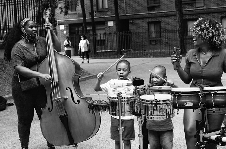 From left, Endea Owens plays upright bass, two young children bang on percussion instruments, and Negah Santos plays percussion.